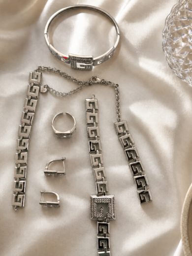 Découvrez la Parure Impériale Argentée™. Un ensemble complet comprenant collier, bracelets, bague et boucles d'oreilles au design luxueux inspiré de l'architecture grecque moderne.